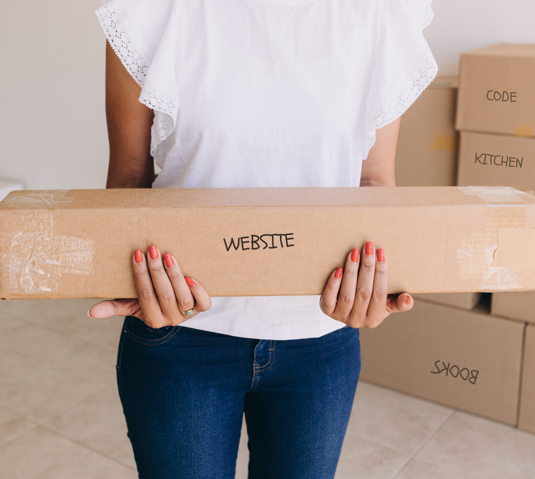 A woman holding a moving box labeled website. In the background are stacked moving boxes labeled code, kitchen, and books.