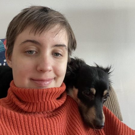 A young white woman with short hair with a dog resting over her shoulder
