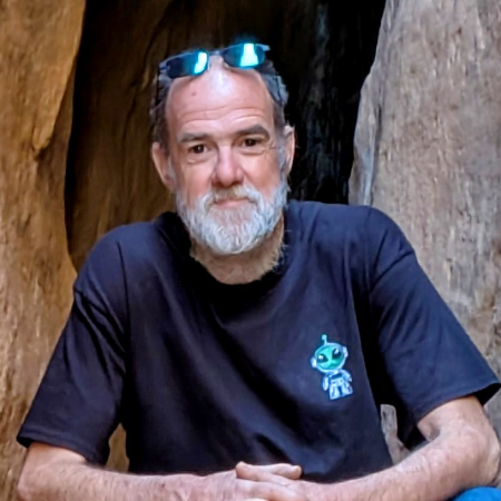A white bearded man wearing sunglasses posing in front of a rock formation
